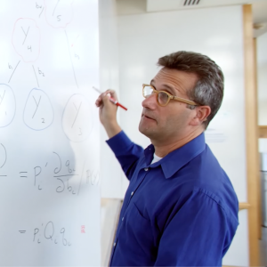 Two people working equations on whiteboard
