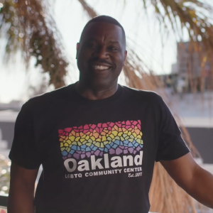 Joe Hawkins standing outside wearing a "Oakland LGBTQ community center" tshirt.