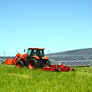 Large red tractor mowing a field next to a solar farm.