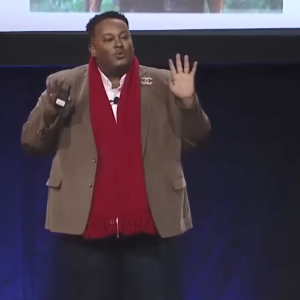 Omar on stage. A large screen behind them.