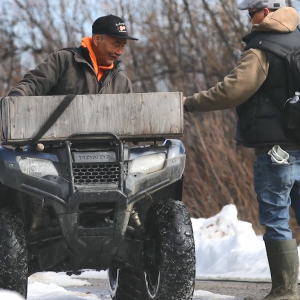 A person hand a package to another on an atv.