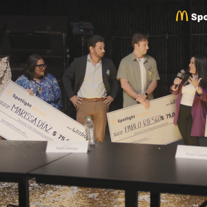 Three winners and presenters in a room each holding large checks.
