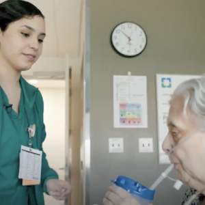 A nurse is assisting a patient with a beverage.