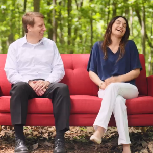 Two people on a red couch in a forested area.
