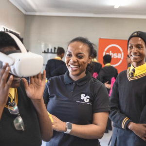 An adult assists school children using a VR headset.