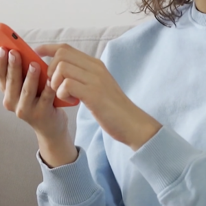 Person wearing a light blue sweater, holding a mobile phone with an orange phone case