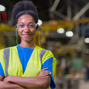 Person smiling with their arms folded, wearing safety glasses and a hi-vis vest