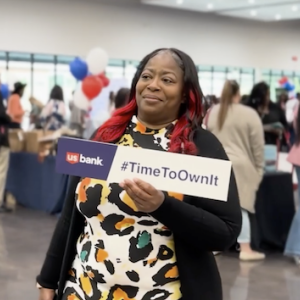 Melody Jones shown at a U.S. Bank location holding a sign that says "Time to Own It".