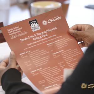 A person holding a schedule of events. Sands logo in the corner.