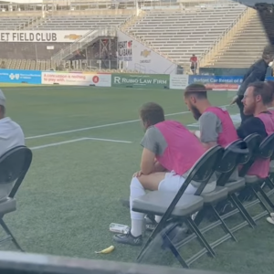 Soccer pitch with people wearing pink vests while sat on foldable chairs