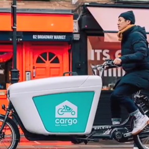 A person on a cargo bike riding past small shops