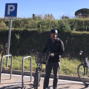 A smiling person standing by a bicycle in a bike parking area.