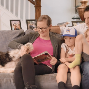 Cara and family seated on a couch reading a book.