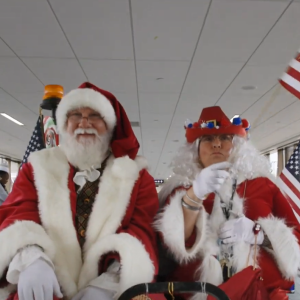 Santa and Mrs. Clause in an airport cart riding down an aisle waving american flags.