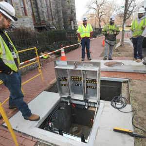 Workers in high-vis clothing and hard hats surround an open hatch in a walkway.