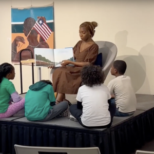 Children sat on the floor while a person shows them an illustrated book 