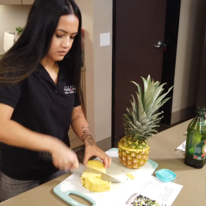 A person chopping a pineapple on a chopping board 