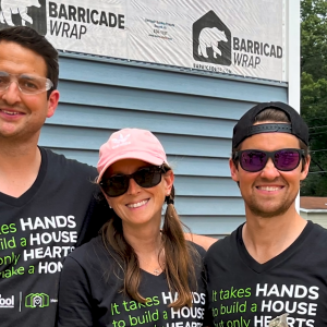 Three volunteers posed in front of a house under construction.