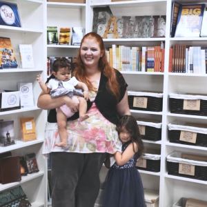 Michaela with two kids standing in front of a bookshelf.