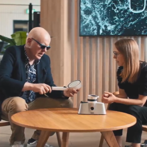 Two people seated at a low table. One holding a shower head.