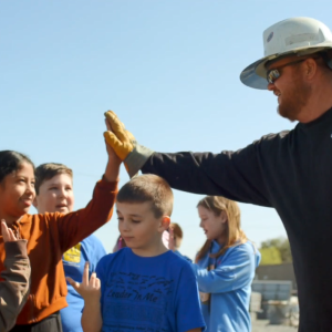 An employee in a hard hat gives a high five to a child.