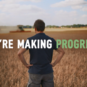"We're Making Progress" over a person, with hands on hips, looking out over a crop field.