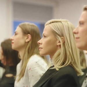 Seated people in a room of others, looking in the same direction.