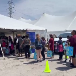 A line of people going under a large white tent. Volunteers standing to the side.