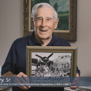 Frank Perry Sr. holding a picture of him and others in uniform by a plane.