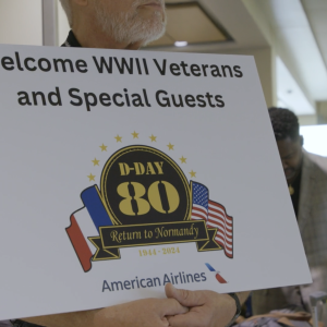 A person holding a sign that reads "Welcome WWII Veterans and Special Guests"