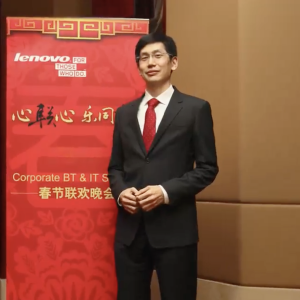 Authur Hu wearing a suit while stood in front of a Lenovo event banner 