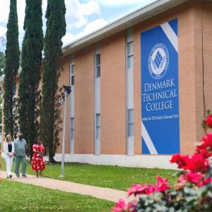 People walking down a sidewalk next to a building "Denmark Technical College" banner on the side.