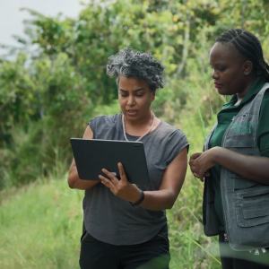 Two people looking at a laptop on a river bank.