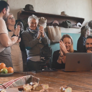 A group of people looking at an open laptop, clapping, in a home setting.