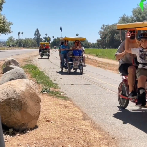 Adults and children riding in covered, pedal-driven carts on a path.
