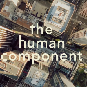 "the human component" over an aerial view of tall city buildings.