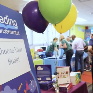 A sign that reads "choose your book!" on an event stand with balloons 