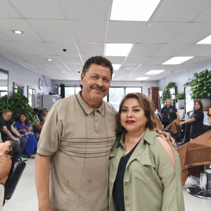 Luz and Juan Andrade standing in a busy barber shop.