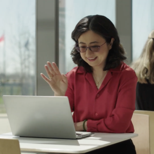 A person sat at a table waving at their laptop