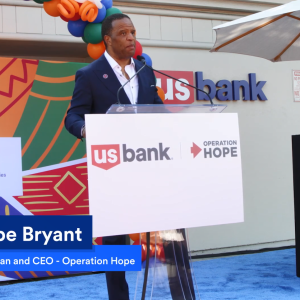 John Hope Bryant speaking at a podium on a stage.