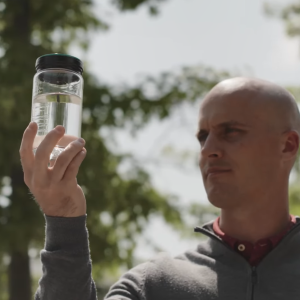 A person holding up a clear bottle of fluid outside.