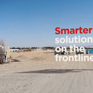 "Smarter solutions on the frontlines" over a sandy area with small buildings in the distance.