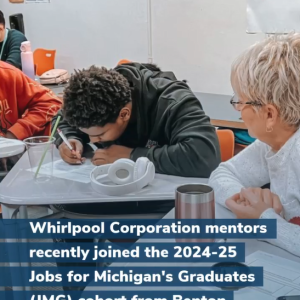 A mentor watching as a student writes at a desk.