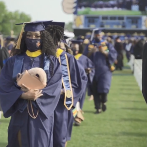 Outside, a line of graduates walking by rows of seated and standing audience members.