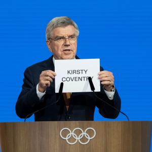Man at lectern holding up s sign reading, "Kirsty Coventry"