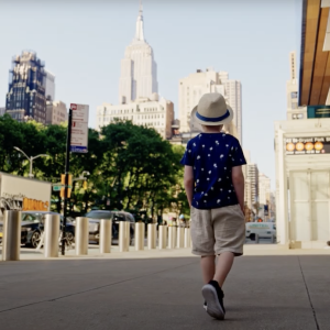 Young boy walking down a street with a hat on.