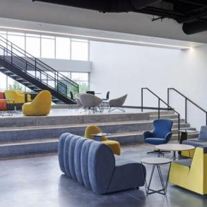 A lobby with blue and yellow seats, which also has a large window looking into a lab