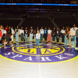 Group of students and professionals standing on the Los Angeles Sparks basketball court for a photo inside Crypto.com Arena.
