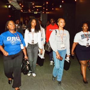 Group of event participants walking together through a Crypto.com Arena corridor, wearing name badges and carrying bags.