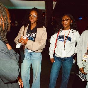 Small group of attendees wearing lanyards engaged in conversation inside an event space at Peacock Theater.